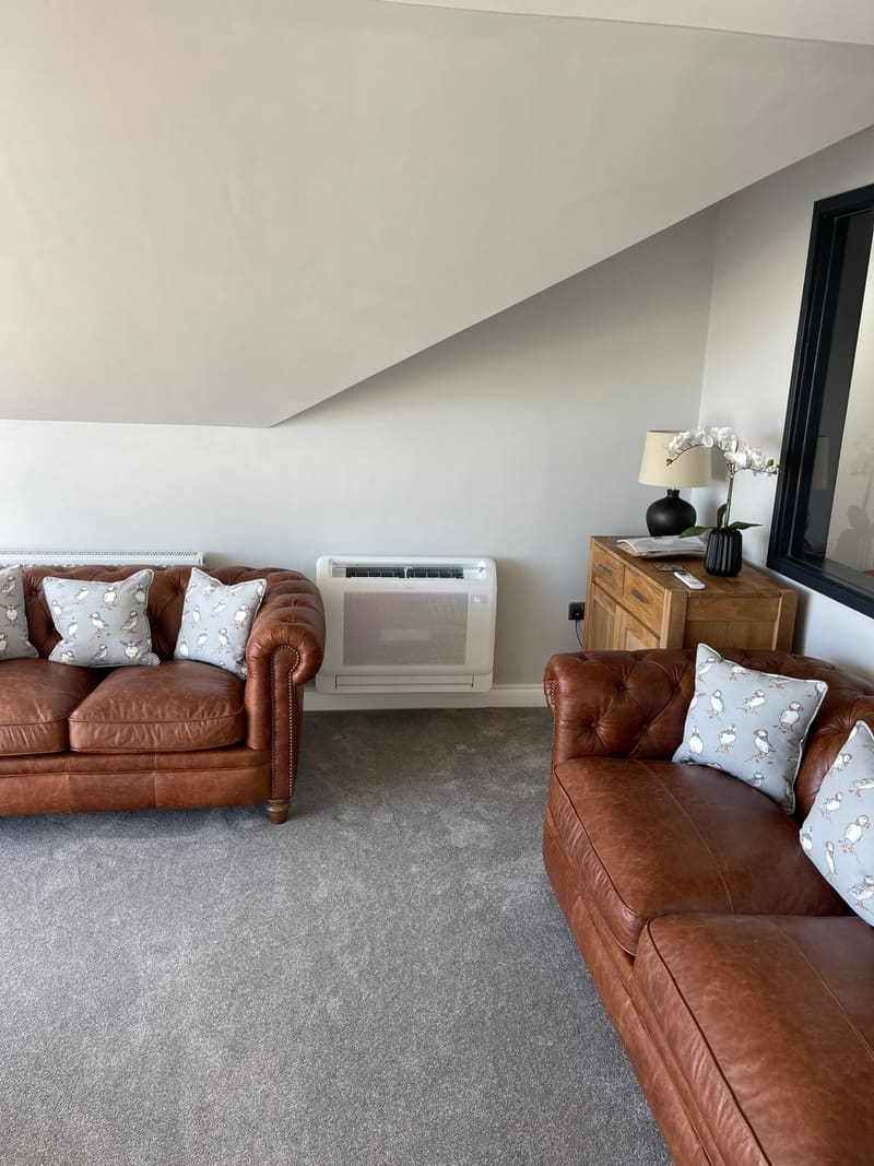 Floor-standing air conditioning console installed in a bright living room with leather sofas