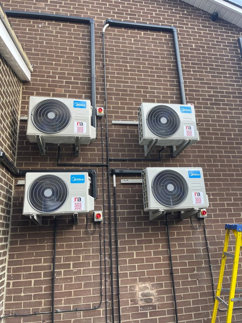 Four outdoor air conditioning units neatly mounted on a brick wall with tidy pipework